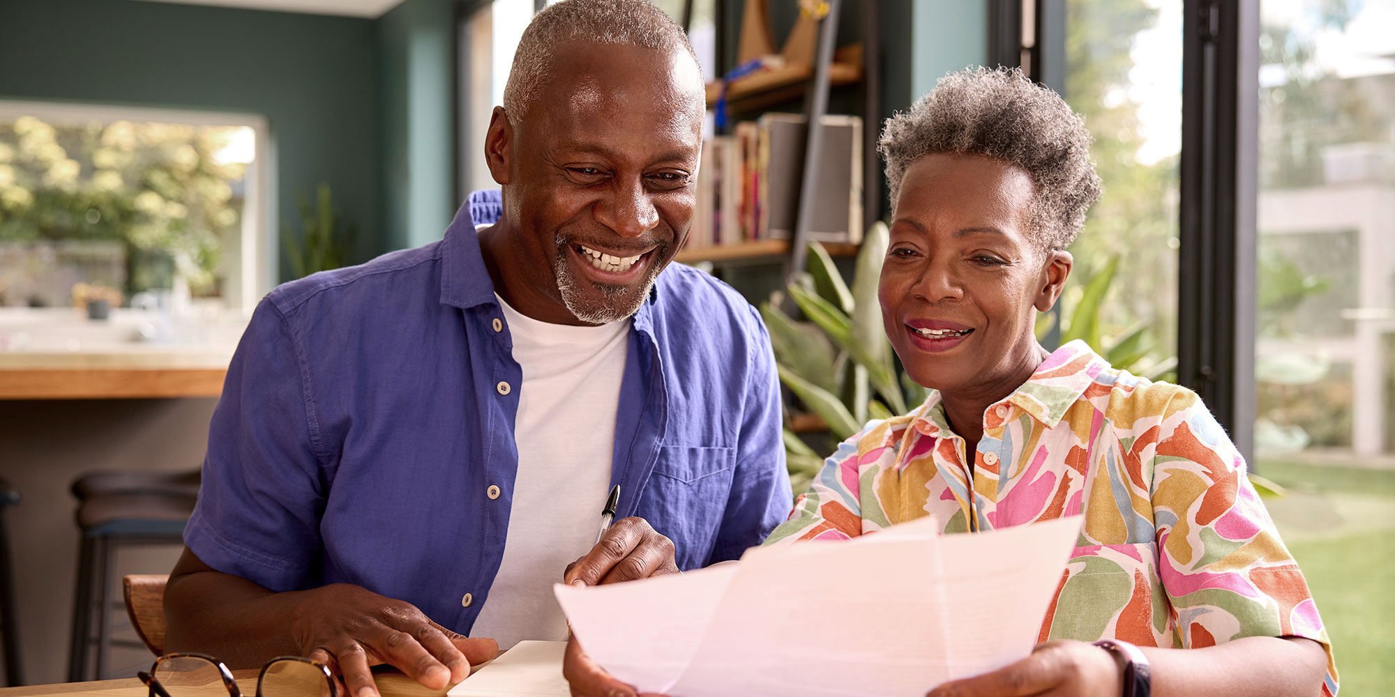 A couple sit together, smiling at papers the woman is holding.