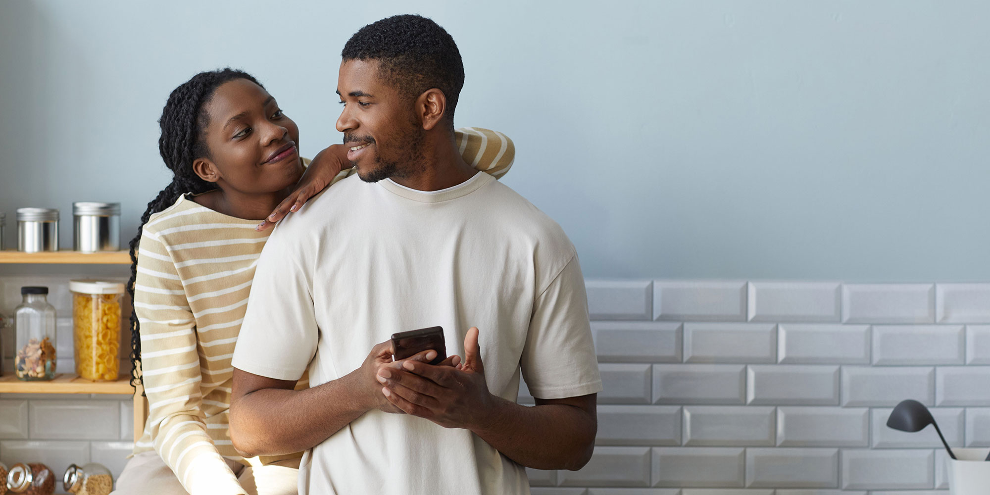 Woman smiling and leaning on man. He is loking at her and smiling and holding a phone in his hand.