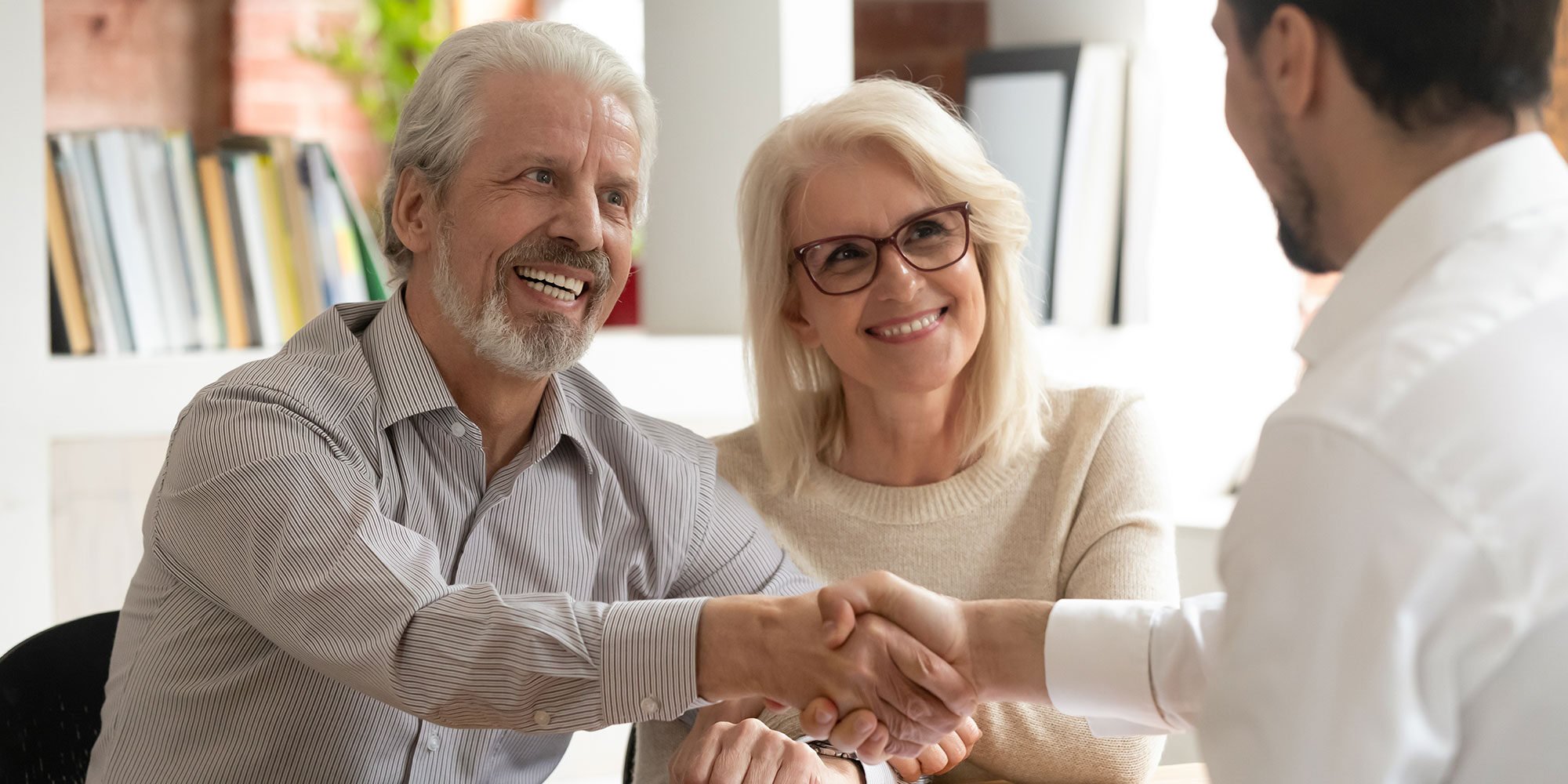 Older couple meeting with financial advisor. Older man is shaking advisor's hand. 