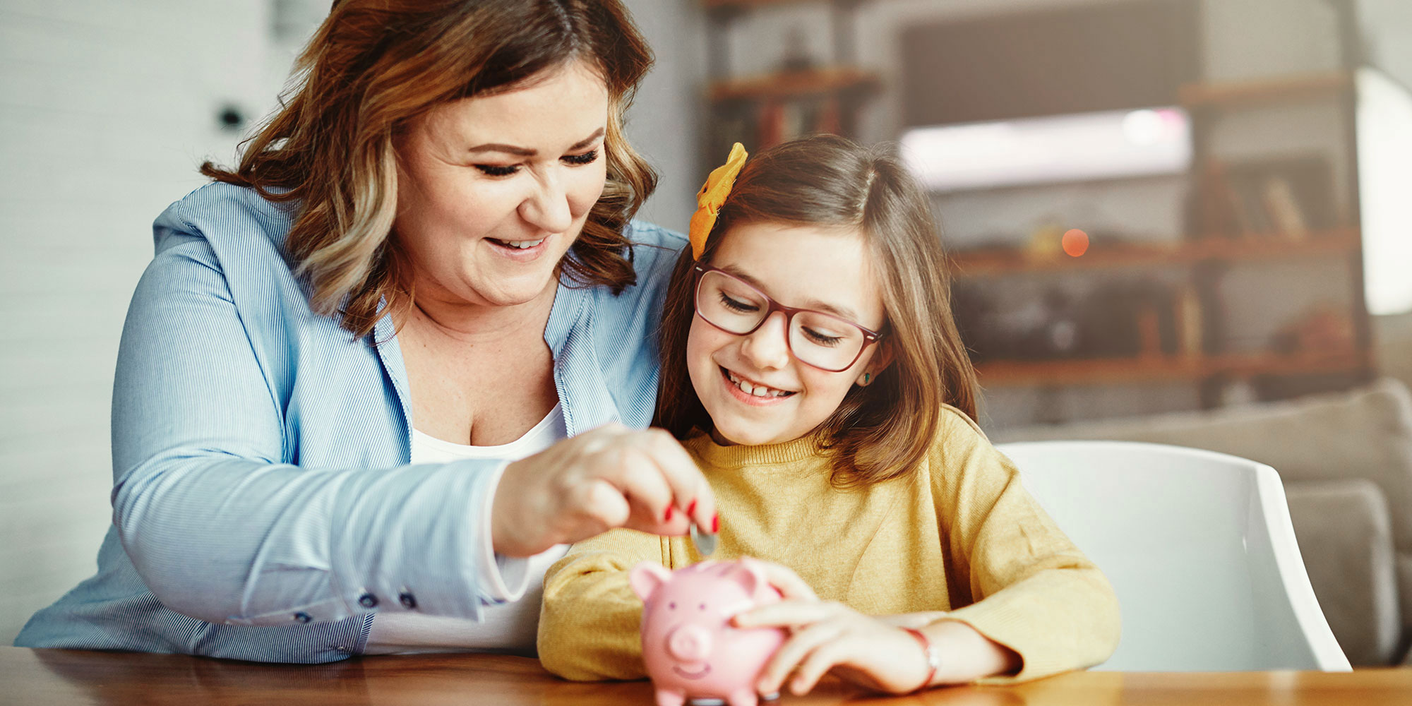 Mother and daughter putting coin inside piggy bank. 