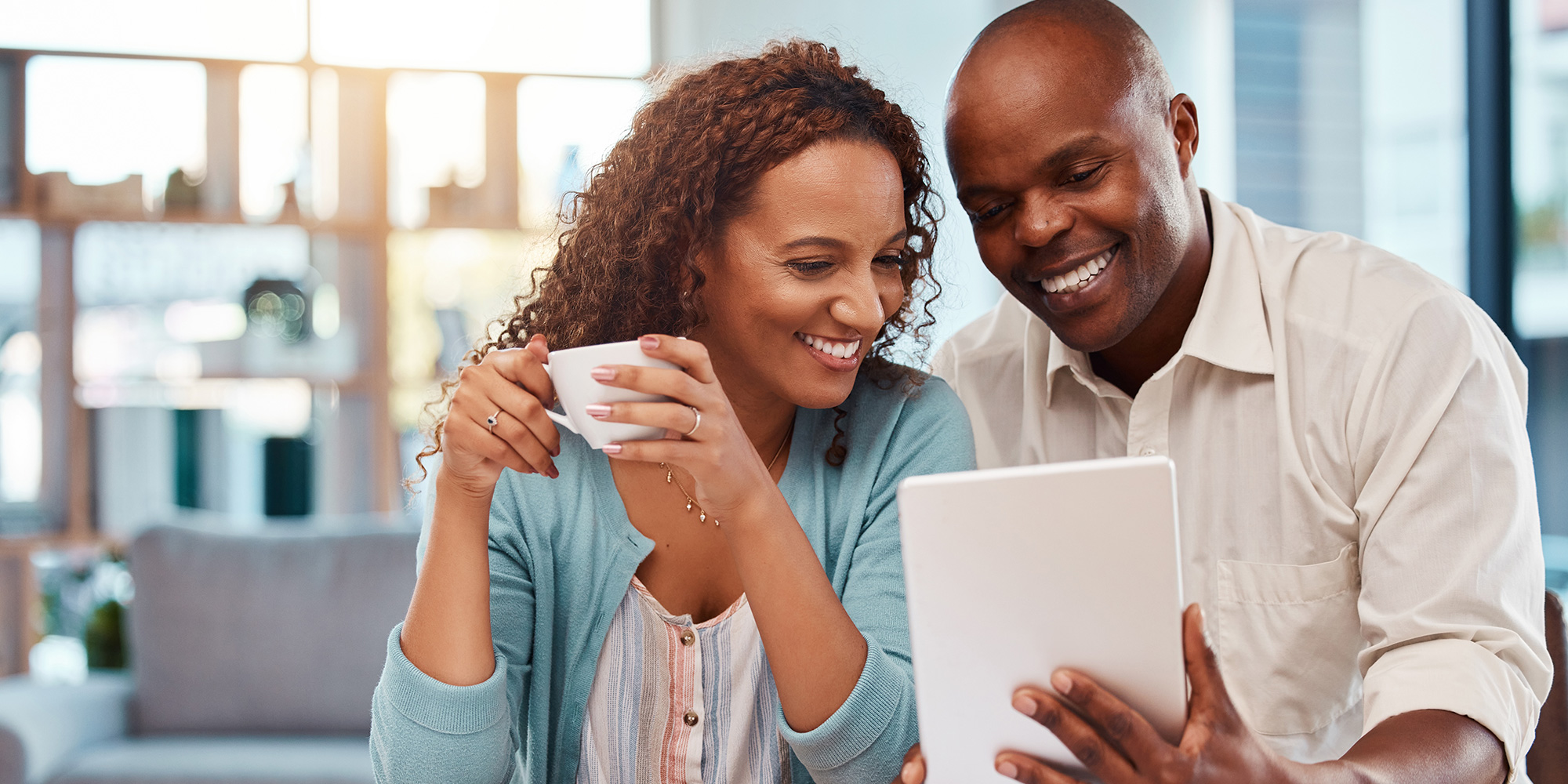 A couple looking at blog on tablet while woman drinks coffee.