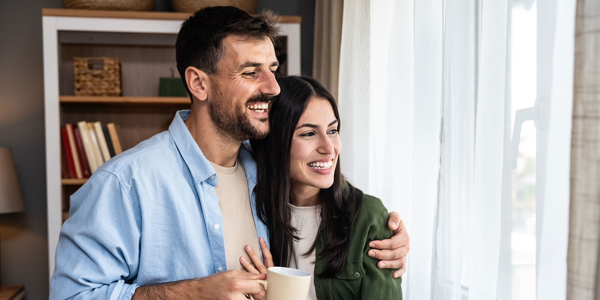 Smiling couple looking outside their window. 