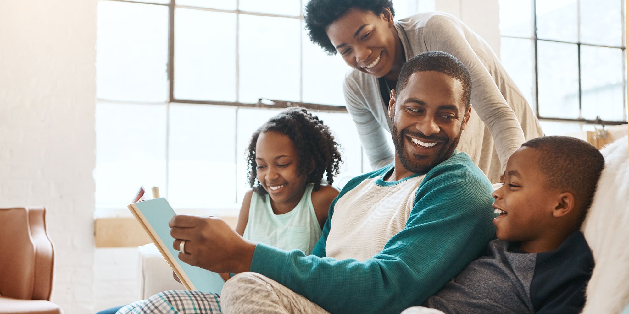 Happy family smiling together, father is reading book to his kids.