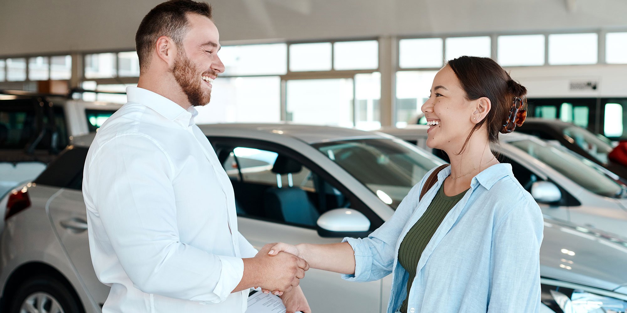 Woman and man shaking hands in front of new car. 